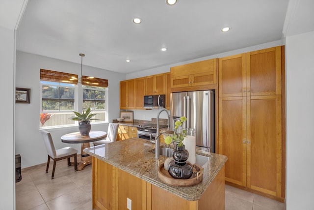 kitchen with light tile patterned floors, stainless steel appliances, light stone countertops, a center island with sink, and decorative light fixtures