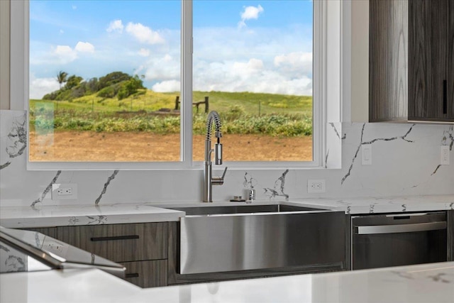 kitchen with sink, backsplash, dark brown cabinets, light stone countertops, and stainless steel dishwasher