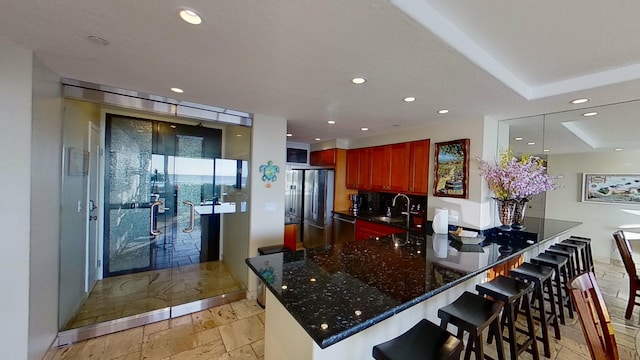 kitchen featuring a kitchen bar, kitchen peninsula, dark stone counters, stainless steel appliances, and sink