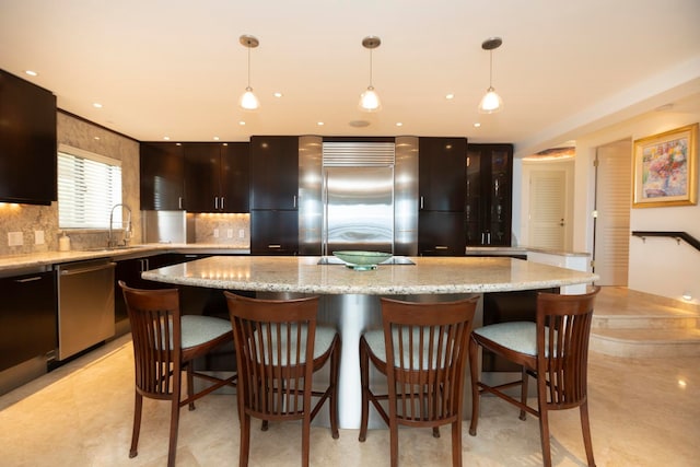 kitchen featuring light stone countertops, backsplash, sink, stainless steel appliances, and a center island