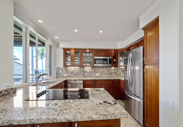 kitchen featuring light stone counters, stainless steel appliances, tasteful backsplash, glass insert cabinets, and a sink