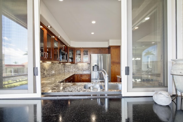 kitchen featuring stone counters, stainless steel appliances, tasteful backsplash, glass insert cabinets, and a sink