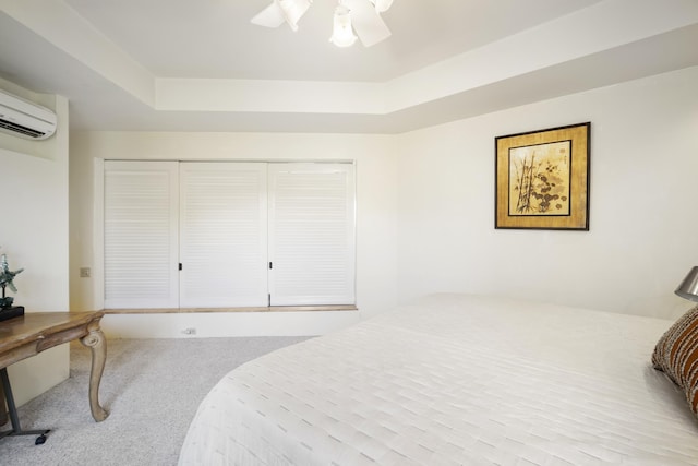 carpeted bedroom with a tray ceiling, a closet, a wall mounted air conditioner, and ceiling fan