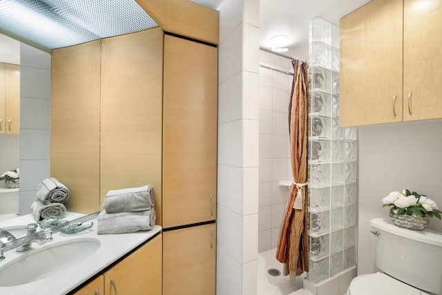 bathroom featuring a tile shower, vanity, and toilet