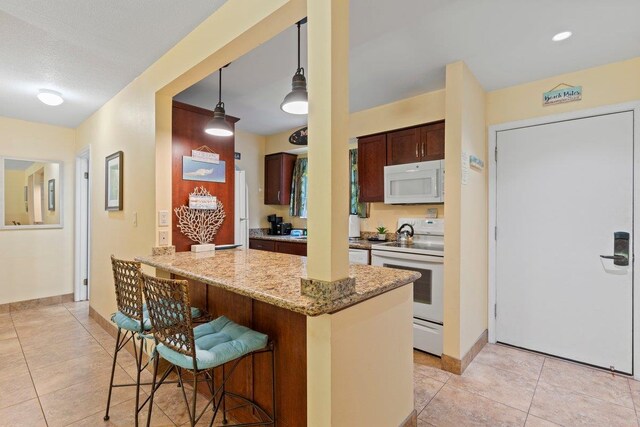 kitchen with light stone countertops, white appliances, kitchen peninsula, a kitchen bar, and decorative light fixtures