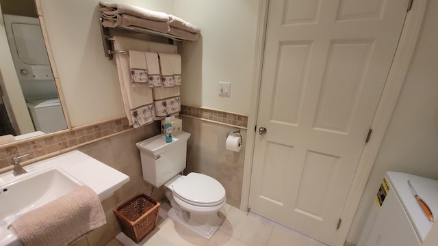 bathroom with tile patterned floors, toilet, tile walls, and stacked washer and clothes dryer