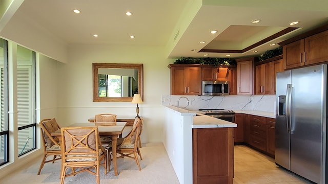 kitchen with kitchen peninsula, appliances with stainless steel finishes, tasteful backsplash, a raised ceiling, and light tile patterned floors