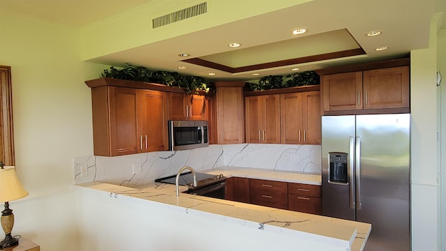 kitchen with decorative backsplash, kitchen peninsula, stainless steel appliances, and a tray ceiling