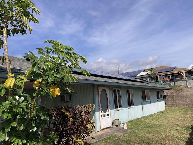 back of house featuring fence, roof with shingles, roof mounted solar panels, and a lawn