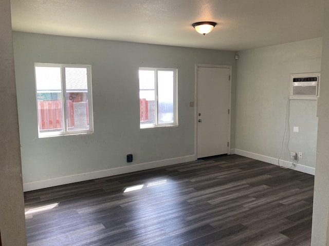 spare room featuring dark wood-style flooring, a wall unit AC, and baseboards