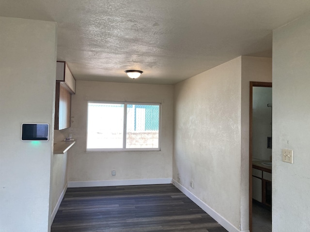 empty room featuring a textured ceiling, dark wood finished floors, and baseboards
