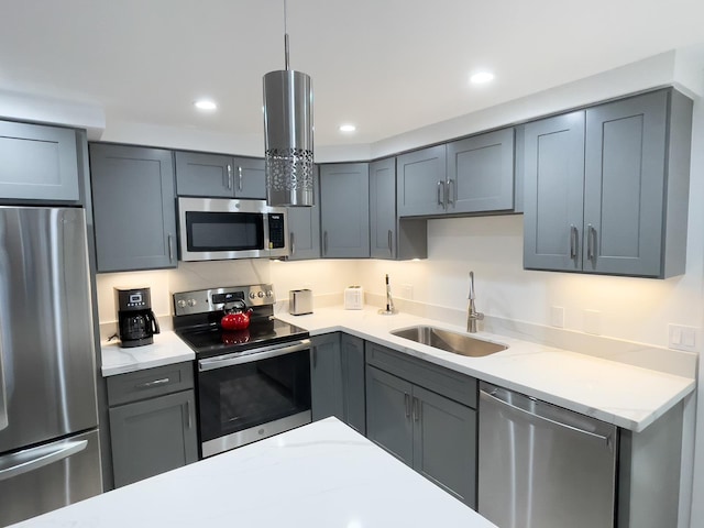 kitchen featuring appliances with stainless steel finishes, light stone counters, decorative light fixtures, gray cabinets, and sink