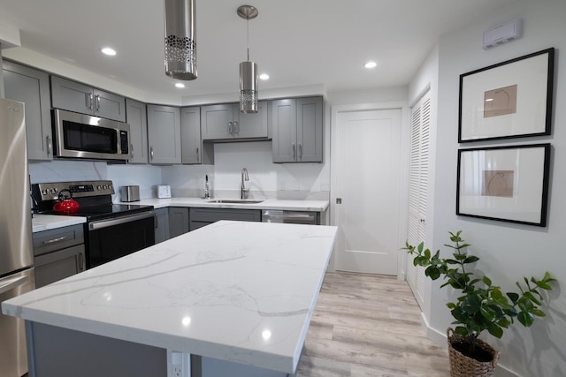 kitchen with appliances with stainless steel finishes, gray cabinetry, decorative light fixtures, a kitchen island, and sink