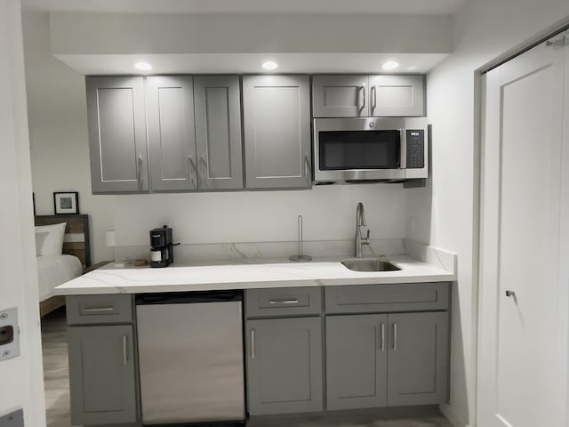 kitchen featuring sink, gray cabinetry, light stone countertops, and dishwashing machine