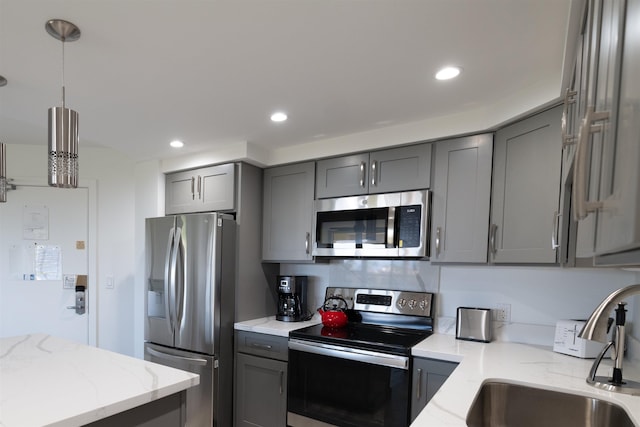 kitchen featuring pendant lighting, stainless steel appliances, gray cabinets, and light stone countertops