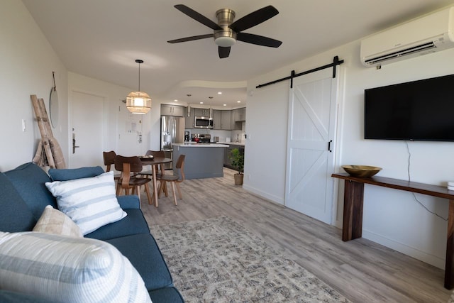 living room featuring a wall mounted air conditioner, light hardwood / wood-style flooring, a barn door, and ceiling fan