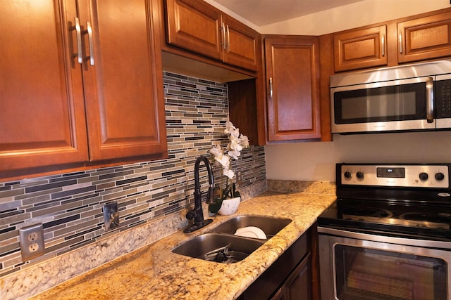 kitchen featuring brown cabinets, decorative backsplash, a sink, appliances with stainless steel finishes, and light stone countertops