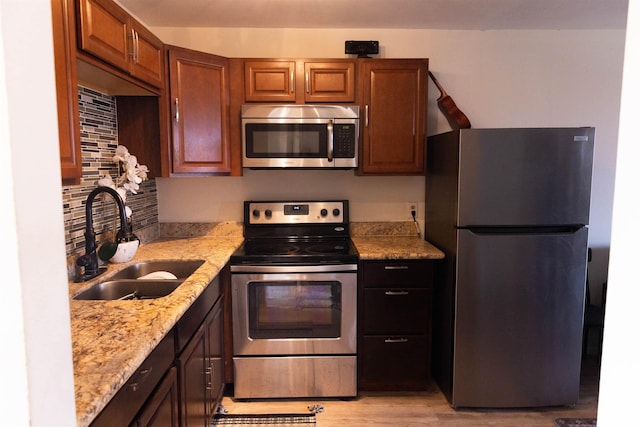 kitchen featuring light stone countertops, a sink, stainless steel appliances, light wood-style floors, and tasteful backsplash