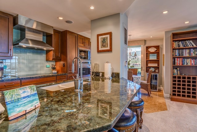 kitchen featuring built in microwave, wall chimney exhaust hood, black electric cooktop, a kitchen breakfast bar, and oven