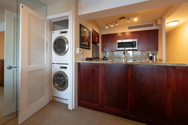 laundry room with stacked washer and clothes dryer, carpet, track lighting, and sink