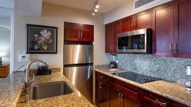 kitchen with light stone countertops, appliances with stainless steel finishes, track lighting, tasteful backsplash, and sink