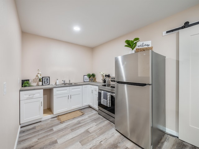 kitchen featuring a barn door, sink, light hardwood / wood-style flooring, appliances with stainless steel finishes, and white cabinets