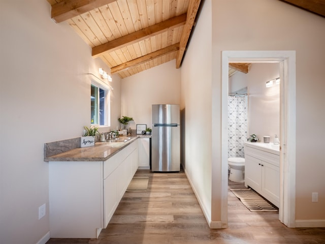 kitchen featuring white cabinetry, wood ceiling, stainless steel fridge, vaulted ceiling with beams, and sink