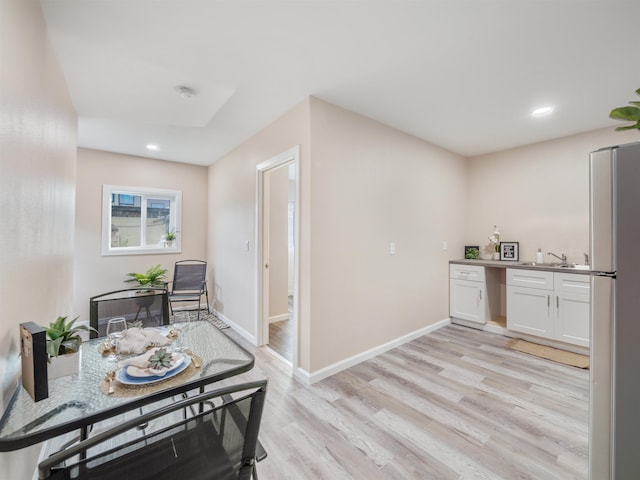 kitchen with white cabinets, stainless steel fridge, sink, and light hardwood / wood-style floors