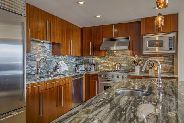 kitchen featuring hanging light fixtures, appliances with stainless steel finishes, dark stone counters, and exhaust hood