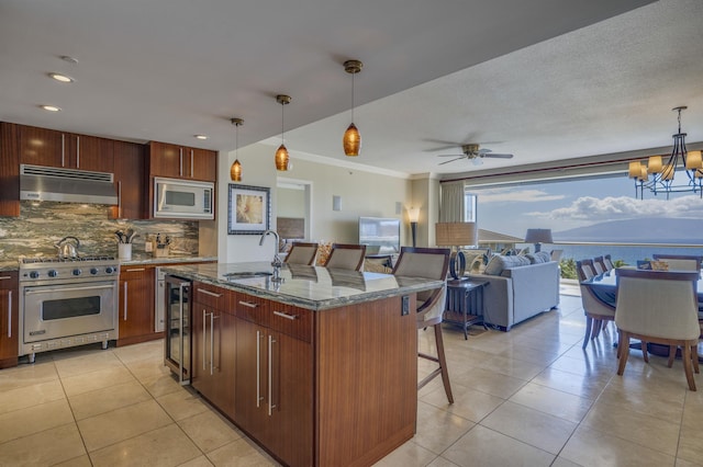 kitchen featuring a center island with sink, stainless steel appliances, hanging light fixtures, open floor plan, and under cabinet range hood