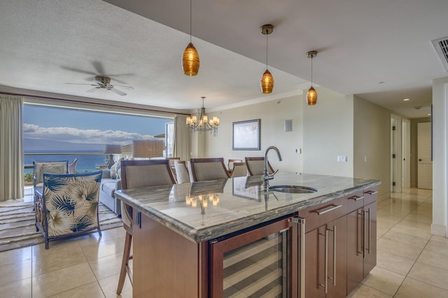 kitchen featuring wine cooler, decorative light fixtures, a breakfast bar, a sink, and a center island with sink