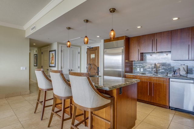 kitchen featuring visible vents, an island with sink, appliances with stainless steel finishes, decorative light fixtures, and a sink