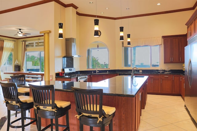 kitchen with an island with sink, dark stone countertops, island exhaust hood, ornamental molding, and stainless steel appliances