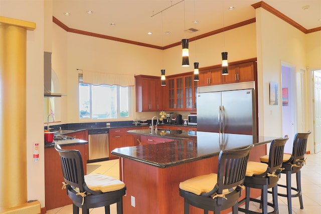 kitchen featuring appliances with stainless steel finishes, decorative light fixtures, an island with sink, light tile patterned floors, and crown molding