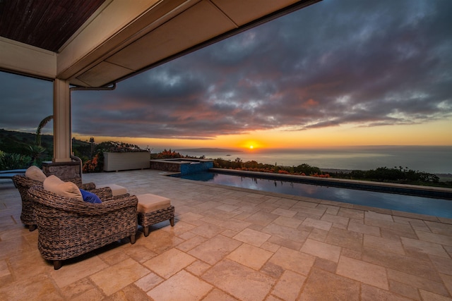 patio terrace at dusk featuring an in ground hot tub and a water view