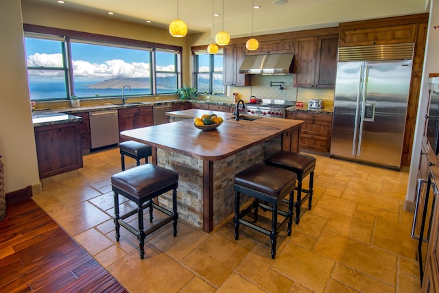 kitchen with sink, backsplash, stainless steel appliances, a center island with sink, and decorative light fixtures