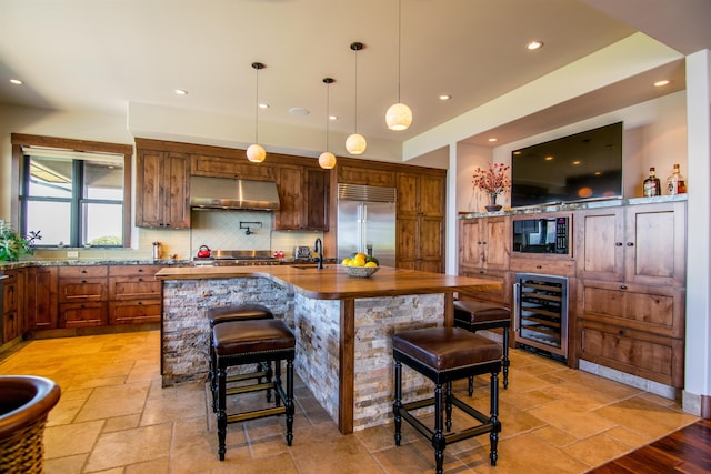 kitchen featuring sink, a breakfast bar area, beverage cooler, a kitchen island with sink, and built in appliances