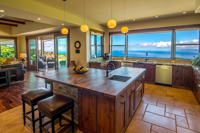 kitchen with hanging light fixtures, dishwasher, sink, and an island with sink