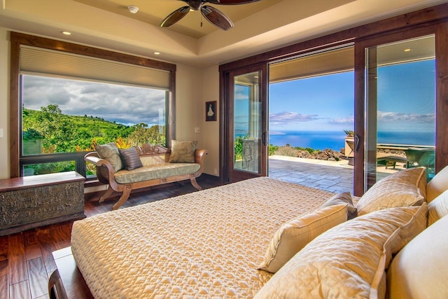 bedroom featuring a water view, a tray ceiling, dark hardwood / wood-style flooring, and access to outside