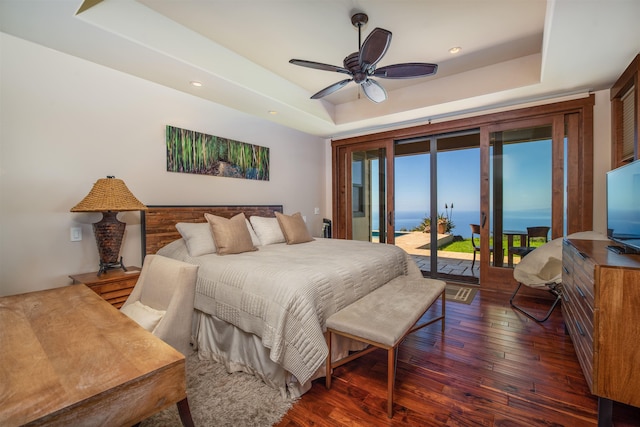 bedroom with dark hardwood / wood-style floors, access to outside, a raised ceiling, and ceiling fan