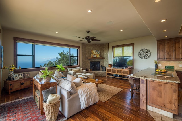 living room featuring ceiling fan, a large fireplace, and dark hardwood / wood-style floors