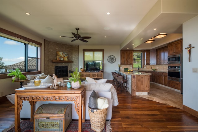 living room featuring a healthy amount of sunlight, dark wood-type flooring, a large fireplace, and ceiling fan