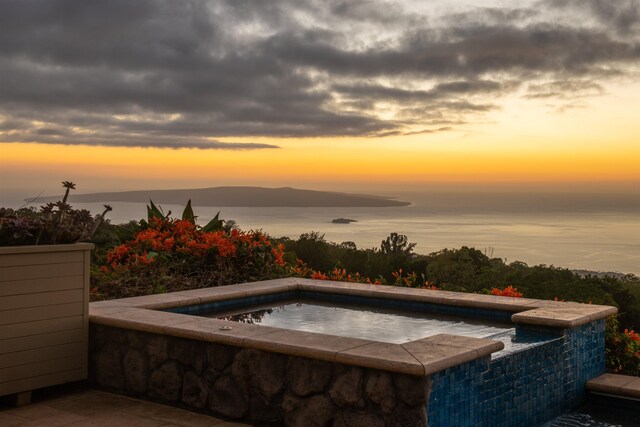 pool at dusk featuring a water and mountain view and an in ground hot tub