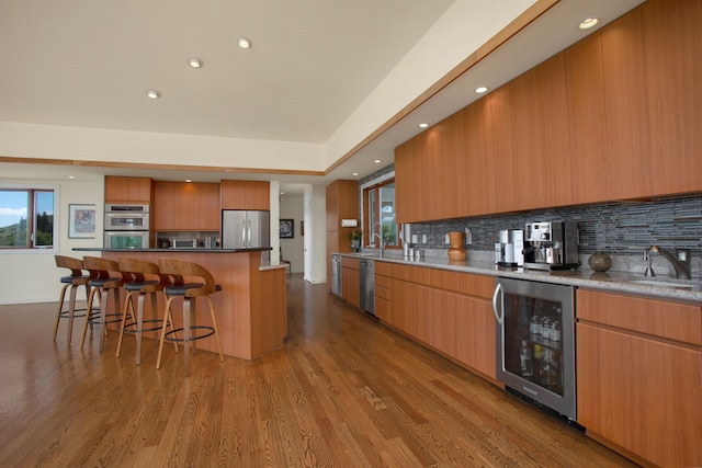 kitchen featuring appliances with stainless steel finishes, a center island, wine cooler, sink, and light wood-type flooring