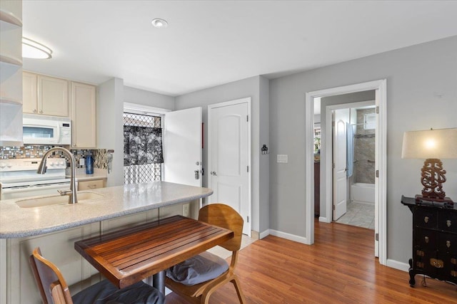 kitchen featuring sink, white appliances, light stone counters, decorative backsplash, and light wood-type flooring