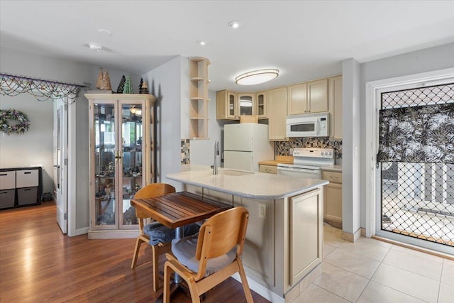 kitchen featuring a breakfast bar area, tasteful backsplash, light tile patterned floors, white appliances, and cream cabinets