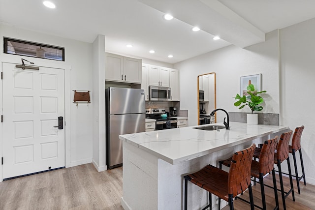 kitchen with a breakfast bar area, light hardwood / wood-style flooring, appliances with stainless steel finishes, kitchen peninsula, and sink