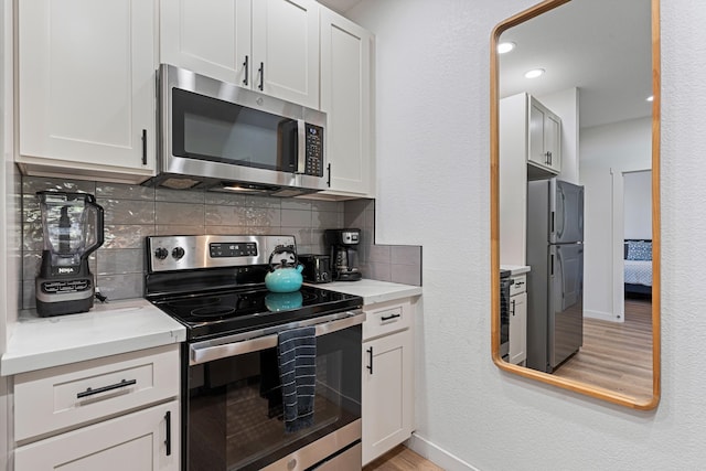 kitchen featuring white cabinets, light hardwood / wood-style flooring, stainless steel appliances, and decorative backsplash