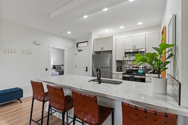 kitchen featuring light wood-type flooring, appliances with stainless steel finishes, light stone counters, sink, and a kitchen bar