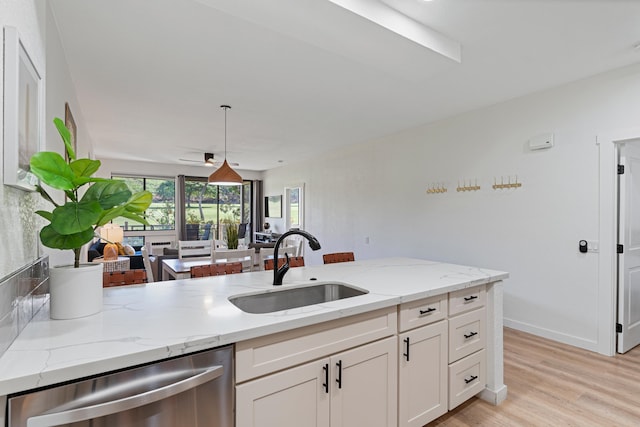 kitchen with light wood-type flooring, decorative light fixtures, dishwasher, light stone counters, and sink